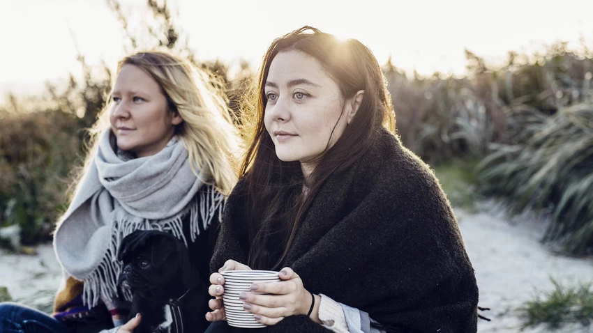 thoughtful-female-friends-sitting-with-dog-on-beach
