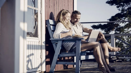 Smiling couple using laptop while having breakfast at porch